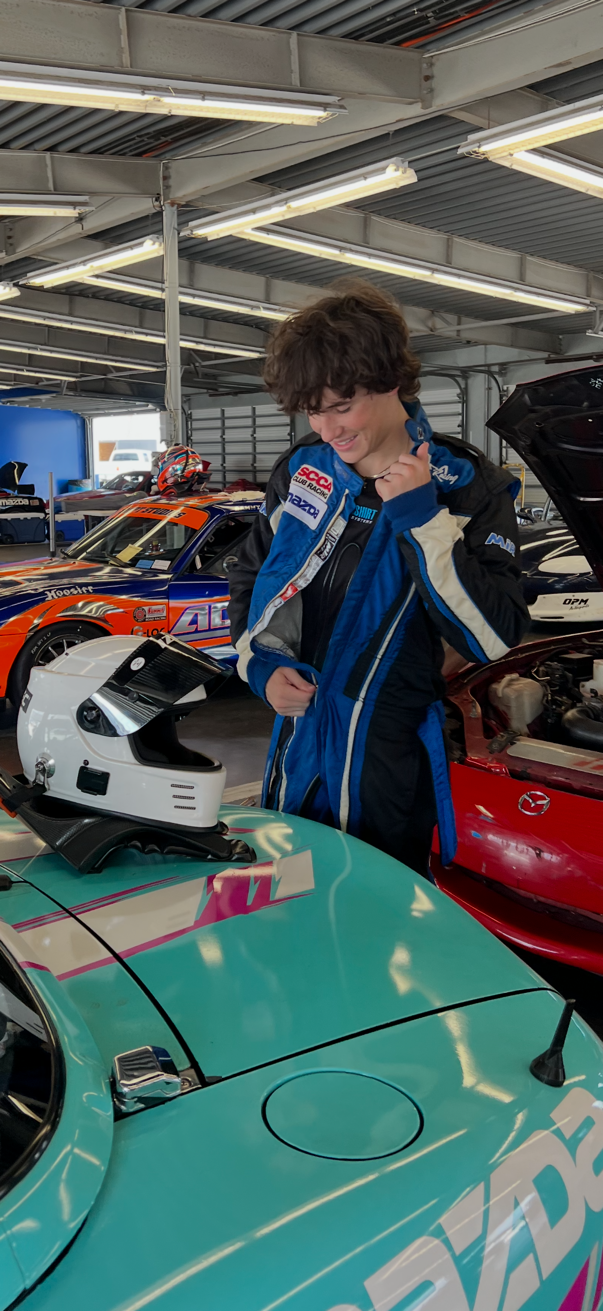 Hayden Kasmen suiting up in the garage next to his OPM Racing Spec Miata