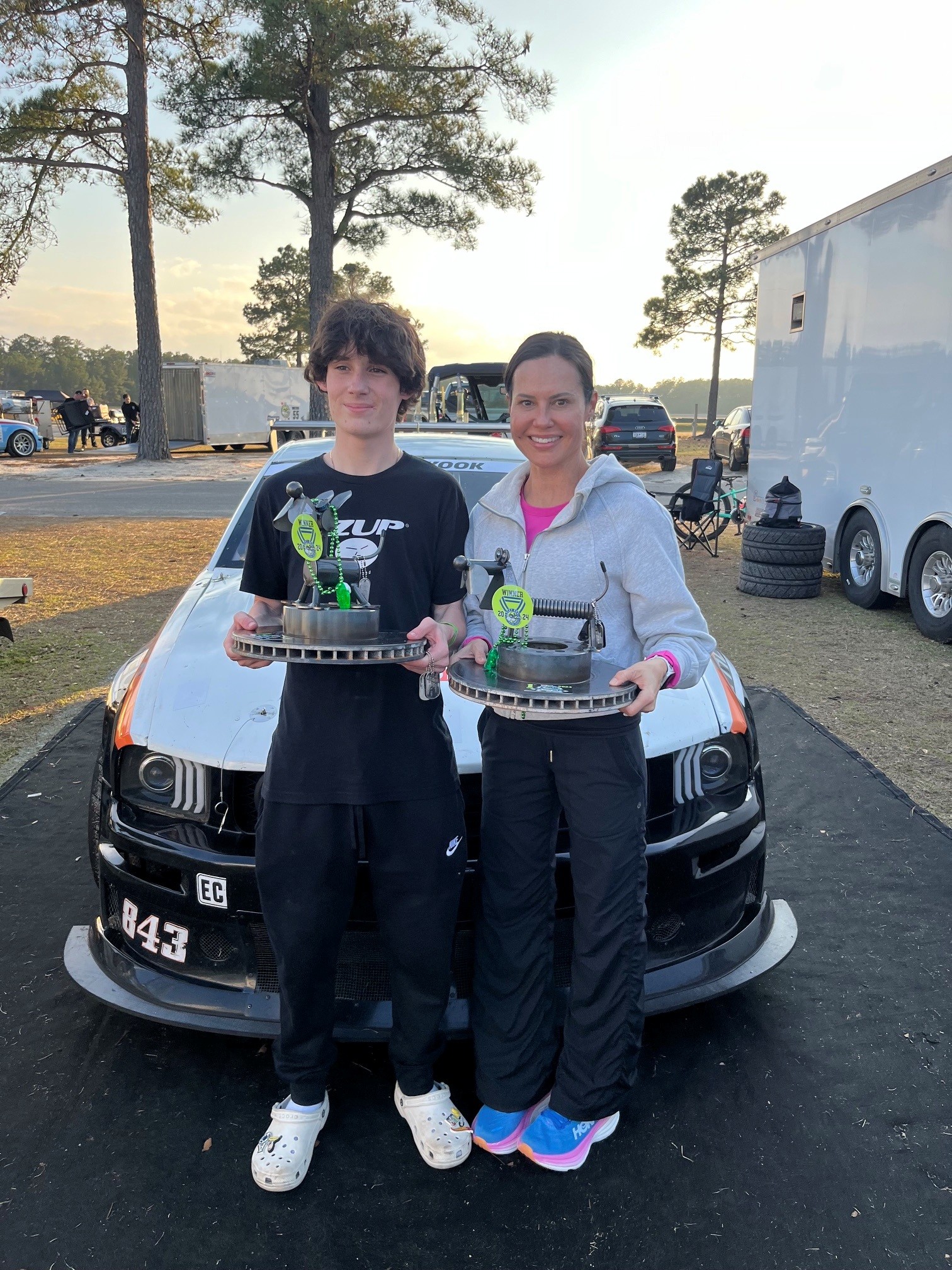 Hayden and his mom holding winner's trophies in front of the No. 843 Mustang