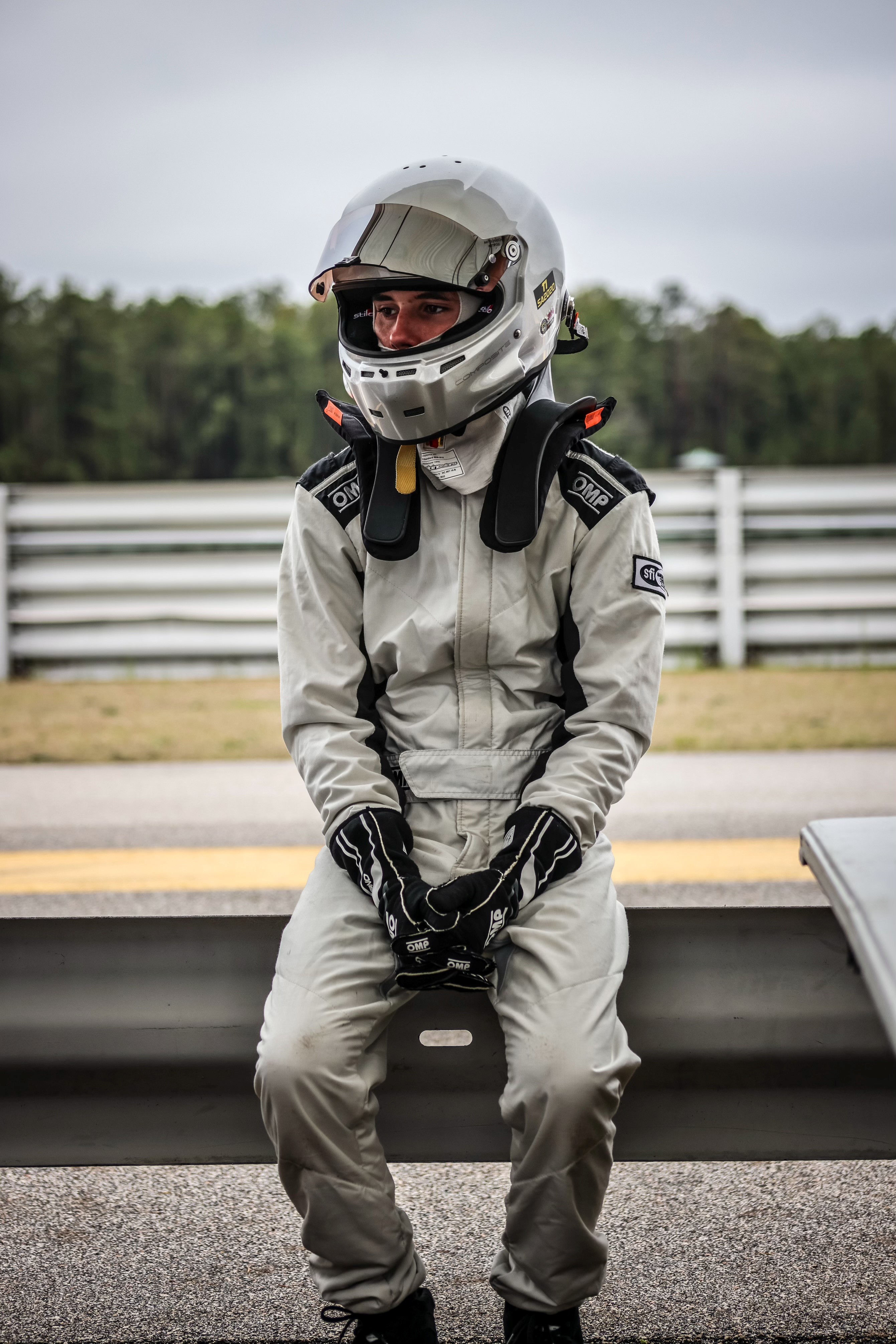 Hayden in his racing suit and helmet sitting on a guardrail trackside