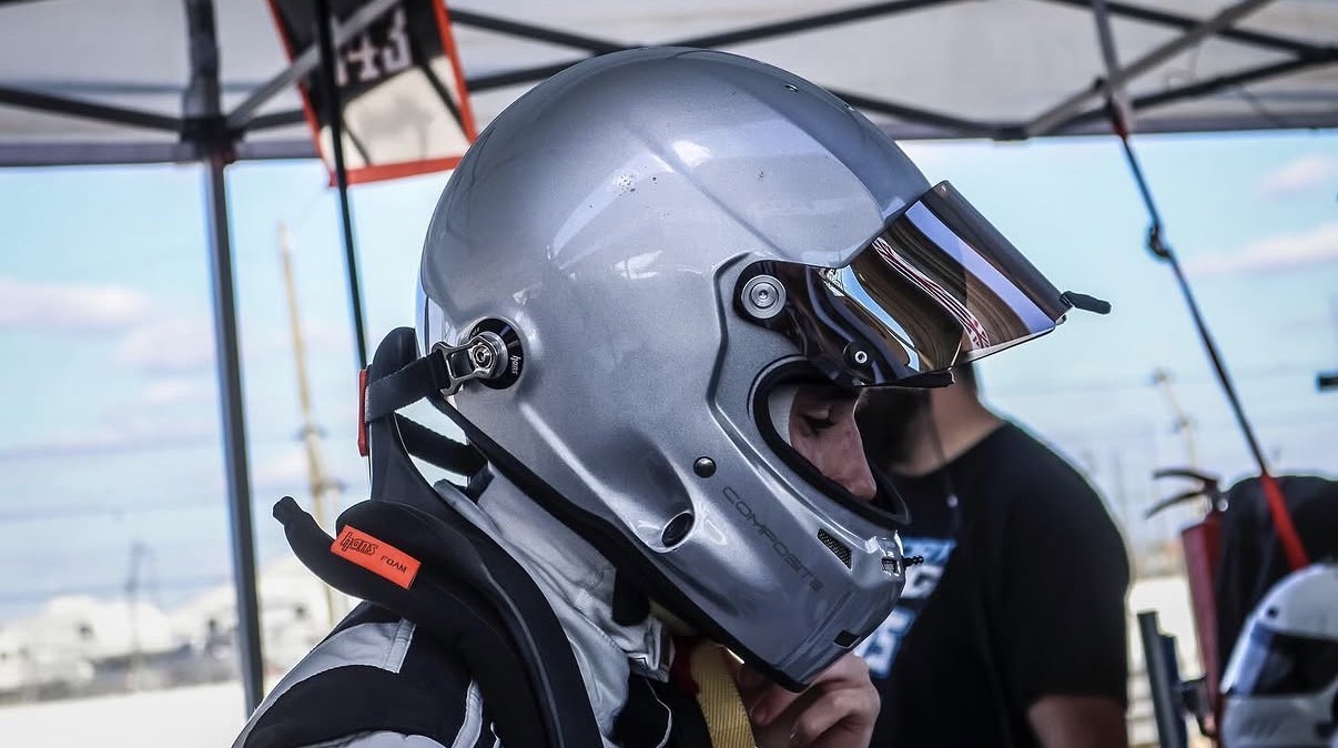 Driver putting on a silver racing helmet trackside